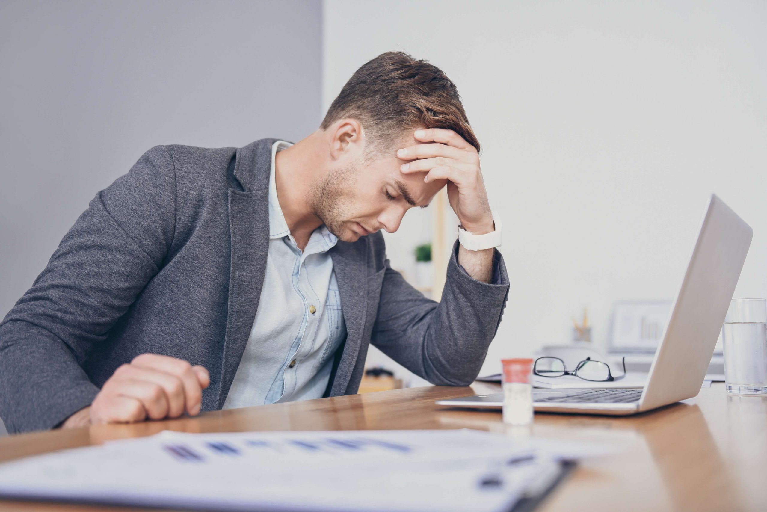 Tired young man using laptop and having headache.